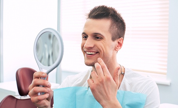 Man smiling in mirror at dental bonding in Rockwall results