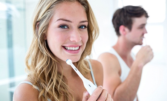 Woman smiling while brushing her teeth in bathroom