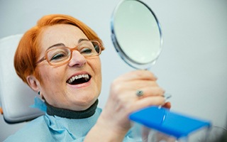 A senior woman admiring her dentures in a hand mirror