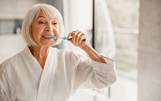 Woman brushing her teeth and preventing dental emergencies in Rockwall