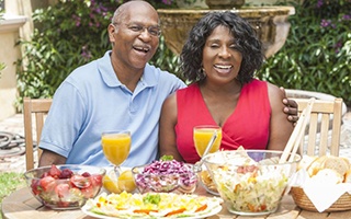 man and woman sitting at a table with various foods and beverages 