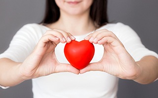 woman holding a red love heart in front of her chest 