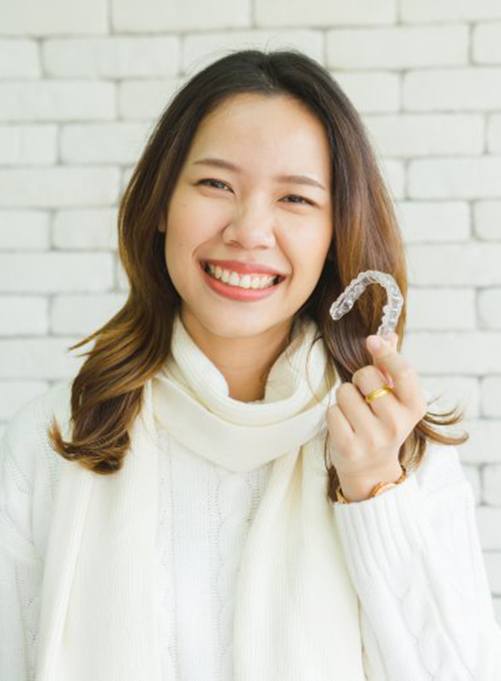 woman in white sweater holding Invisalign in Rockwall 