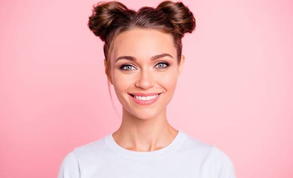 woman with hair in space buns smiling against pink background 