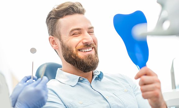 Man smiles in mirror after visiting his cosmetic dentist 