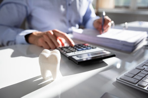 Man with calculator with tooth on desk representing the cost of dentistry