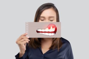 Woman closing her eyes holding a picture of gum disease over her mouth