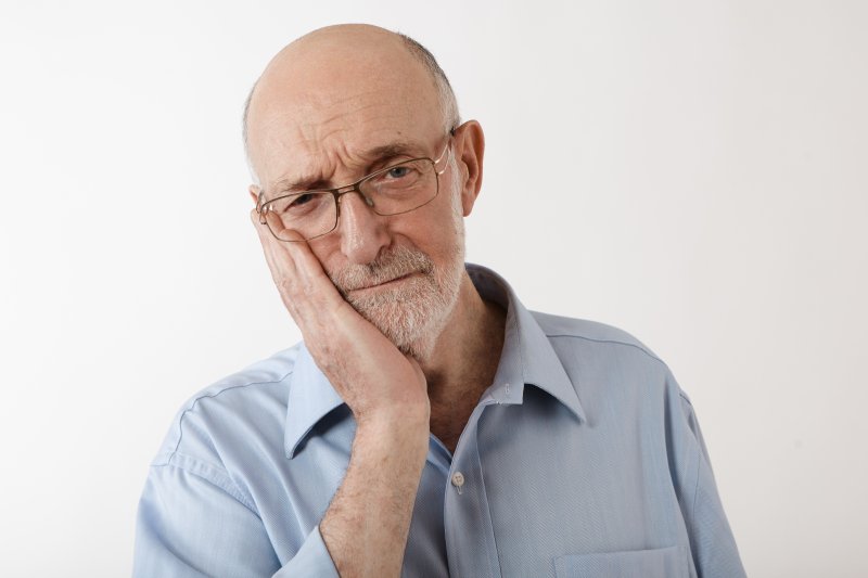 Older man holding his jaw due to poorly fitted dentures