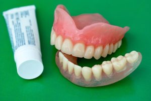Tube of adhesive next to dentures on green surface