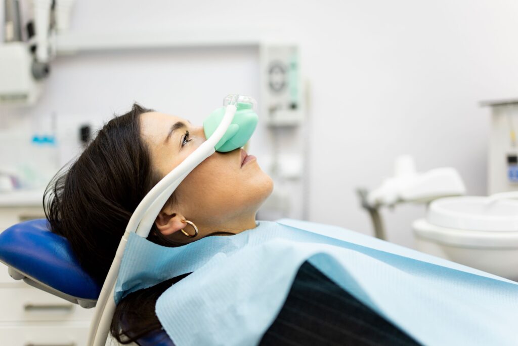 Woman with dark hair in dental chair wearing nitrous oxide mask over nose